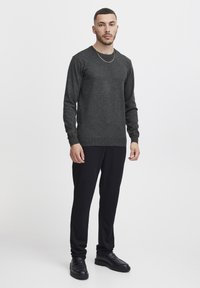Maglione a maglia grigio scuro con maniche lunghe, scollatura rotonda, indossato con pantaloni neri e scarpe nere. Design semplice e aderente con una finitura texturizzata.