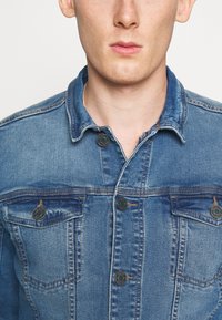 Jeansjacka med en klassisk design, ljusblå färg, knapprad fram, två bröstfickor och strukturerad krage med sömnadsdetaljer.