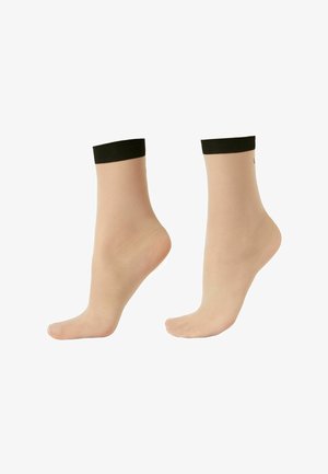 Przezroczyste cieliste skarpetki do kostek z czarnymi elastycznymi ściągaczami, noszone na stopach, jedna stopa płasko, druga uniesiona na palcach.