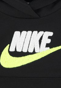 Fekete kapucnis pulóver, amelyen egy hangsúlyos, textúrált fehér "NIKE" logó és egy fényes neon sárga swoosh található, mindkettő a kelme közepén.