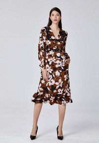 Robe florale marron avec un décolleté en V, des manches longues et un ourlet froncé. Présente des fleurs roses et blanches, des poches latérales et une silhouette ajustée.