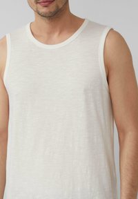 Witte mouwloze tanktop gemaakt van lichtgewicht stof. Heeft een ronde halslijn en een subtiel textuurpatroon. Klein logo nabij de borst.