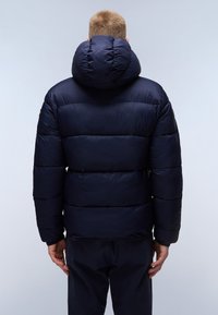 Temno modra puhovka s visokim, voluminoznim kapuco in kvadratnim vzorcem. Ima elastične manšete in prilegajoč spodnji rob za dodatno toploto.