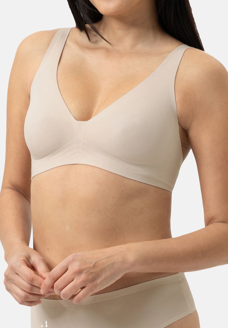 Reggiseno wireless beige con spalline larghe e design a V. Tessuto liscio con una consistenza solida, che offre uno stile minimalista e supporto.