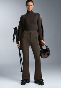 Barna síruha, testhez simuló garbóval és harang szabású nadrággal, gombokkal és cipzáras zsebekkel. Kiegészítők közé tartozik egy sisak és túrabotok.