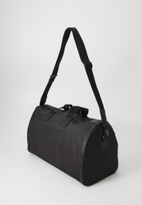 Sac de sport noir avec une surface texturée, deux poignées de transport et une sangle réglable. Doté d'une fermeture éclair et d'une forme arrondie.