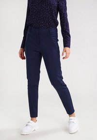 Granatowe spodnie w slim fit wykonane z elastycznej tkaniny, z bocznymi kieszeniami i gładkim wykończeniem, zestawione z białymi sneakersami i wzorzystą bluzką.