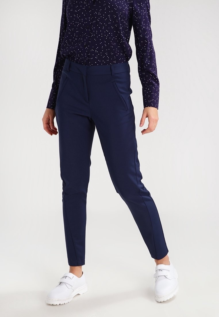 Granatowe spodnie w slim fit wykonane z elastycznej tkaniny, z bocznymi kieszeniami i gładkim wykończeniem, zestawione z białymi sneakersami i wzorzystą bluzką.