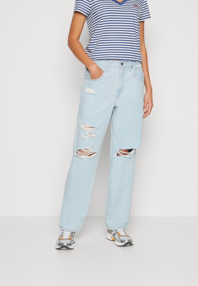 Lysblå denimjeans med slidte detaljer og store huller, parret med en stribet V-hals skjorte og grå sneakers, i en afslappet pasform.