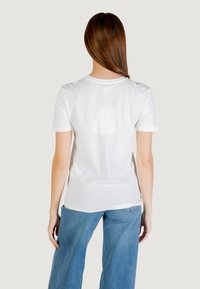 Camiseta blanca de manga corta con cuello redondo, con una textura suave y un corte relajado, combinada con jeans de pierna ancha en azul claro.