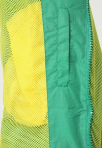 Chaleco de malla en amarillo y verde. Presenta una sección sólida verde con cierre de cremallera y un bolsillo con parche. La textura es ligera y transpirable.