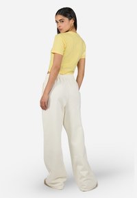 Tricou scurt galben din bumbac, asociat cu pantaloni de trening cremoși, cu talie înaltă și lejeri. Textură netedă, design simplu.