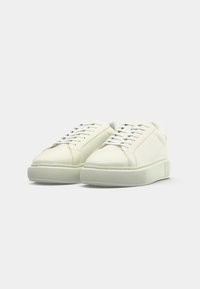 Pair of white low-top sneakers with thick soles and white laces on a plain light background.
