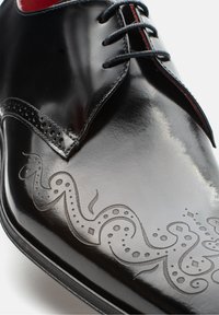 Schwarze, lackierte Leder-Dressschuhe mit dekorativem, eingraviertem Wirbelmuster. Sie verfügen über runde Schnürsenkel und ein kontrastierendes rotes Innenfutter. Flache Sohle.