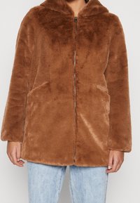 Braune Jacke aus Kunstpelz mit Kapuze, Reißverschluss vorne und zwei Seitentaschen. Weiche Textur und übergroßer Schnitt, mit langen Ärmeln.