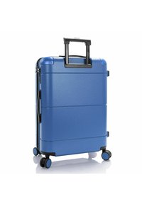 Valise rigide bleue avec une finition lisse, une poignée rétractable, quatre roues et des accents noirs. Présente des lignes horizontales sur la surface.