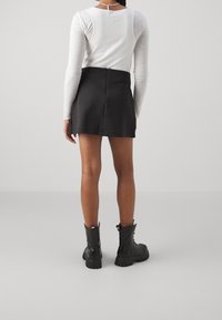 Jupe mini noire avec une texture douce, design ajusté et fermeture éclair à l'arrière. Associée à des bottes en cuir noir montant jusqu'aux genoux avec des semelles robustes.