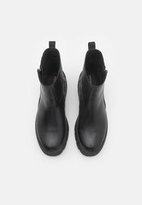 Paire de bottines en cuir noir avec semelles épaisses et fermetures éclair latérales, vues de dessus sur fond blanc.
