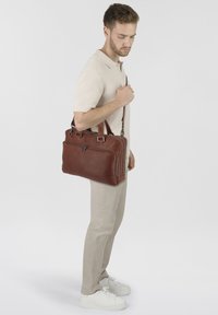 Valigetta in pelle marrone con doppio manico e tracolla removibile, caratterizzata da una texture liscia e una tasca frontale con zip.