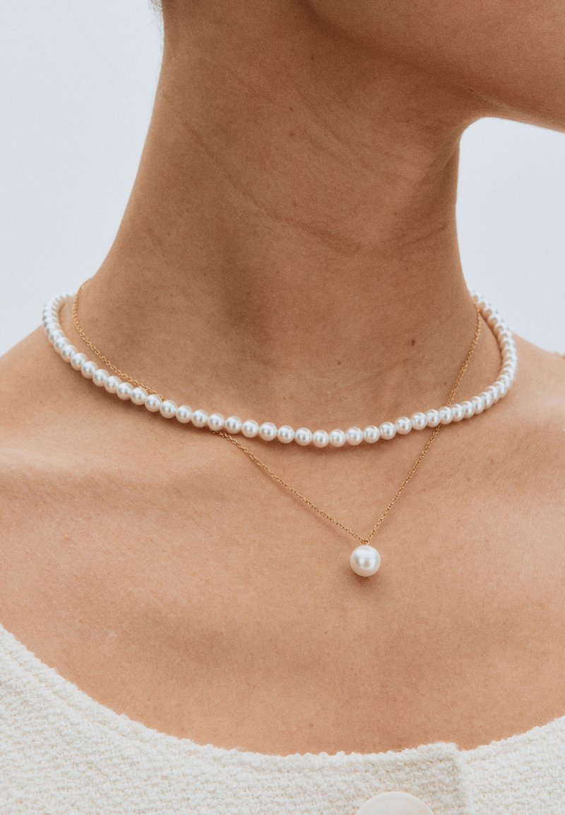 Pearl necklace layered with a gold chain featuring a single pearl pendant; smooth, round pearls in white, delicate gold hardware.