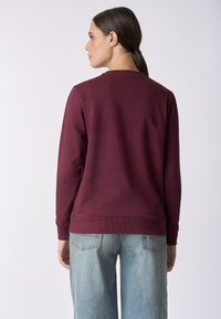 Felpa bordeaux con collo a cisterna, polsini e orlo a costine, realizzata in materiale morbido, abbinata a jeans a gamba larga in denim chiaro.