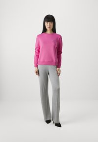 Fuchsia sweatshirt met geribbelde manchetten en halslijn, gecombineerd met lichtgrijze gestreepte broek met wijde pijpen en zwarte puntige hakken.