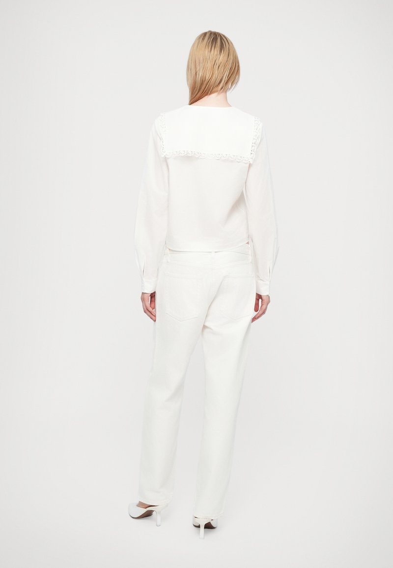 Weiße Bluse mit Spitzenverzierungen auf der Rückseite, ergänzt durch weiße weit geschnittene Jeans. Glatte Textur mit einem klassischen Schnitt.