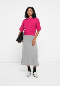 Pull en tricot torsadé fuchsia à manches courtes associé à une jupe maxi grise à côtes. Un sac noir et des mocassins blancs viennent compléter la tenue.