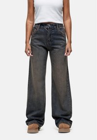 Jean en denim à jambes larges dans un bleu foncé délavé, avec une fermeture à bouton et à glissière, des poches avant et une coupe ample au niveau des chevilles.