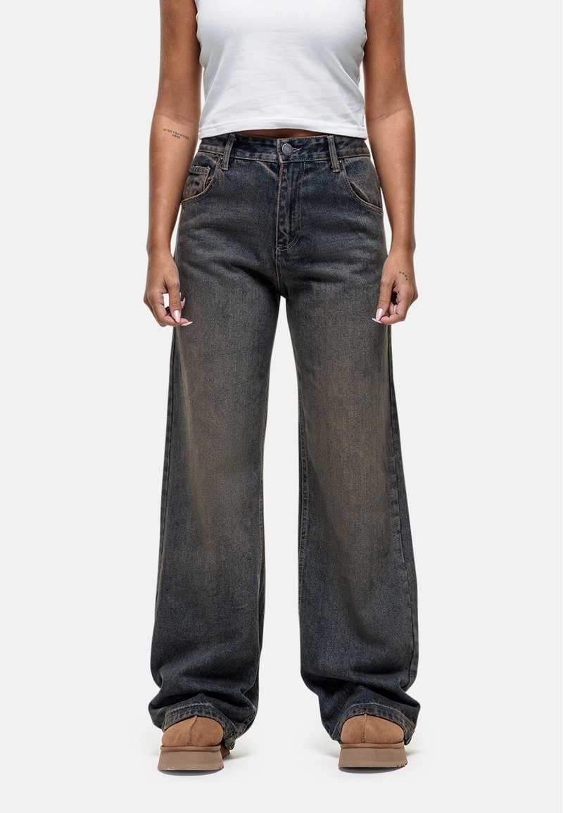 Jean en denim à jambes larges dans un bleu foncé délavé, avec une fermeture à bouton et à glissière, des poches avant et une coupe ample au niveau des chevilles.