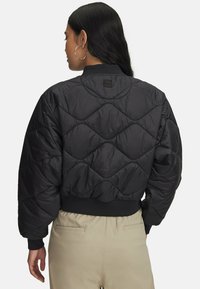 Sort quiltet cropped jakke med diamantmønster, ribbede manchetter og krave, med et logo-patch på ryggen.