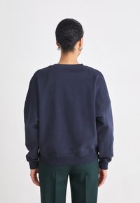 Felpa blu navy con vestibilità comoda, colletto e orlo a coste; presenta spalle scese. Abbinata a pantaloni verdi.