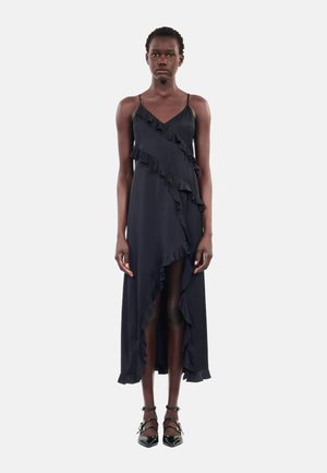 Robe noire sans manches avec des bords volants, un ourlet asymétrique et une texture fluide. Présente des bretelles fines et une fente sur le côté pour une liberté de mouvement.