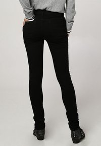 Jean skinny noir à taille haute, avec une texture lisse, des poches arrière et une coupe ajustée. Associé à des bottines noires.