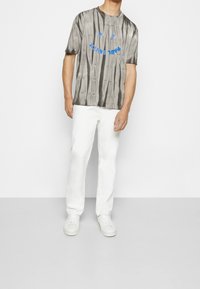 Camiseta de manga corta en tie-dye gris con letras gráficas azules, combinada con pantalones blancos y zapatillas blancas. Textura suave, corte relaxed.