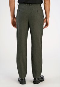 Ciemnozielone wełniane spodnie o fakturowanej powierzchni, prostym kroju nogawek i dwóch tylni pockets, noszone z czarnymi butami.
