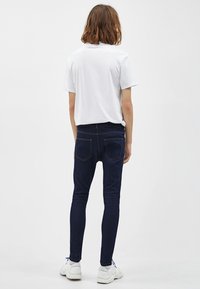 Vit t-shirt med kort ärm kombinerad med mörkblå tajta jeans, med subtila sömsyningar och en minimalistisk design.