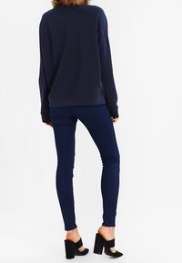 Námořnická mikina s kulatým výstřihem, spárovaná s tmavomodrými slim jeans a černými sandály na klínu s kotníkovými pásky. Hladká textura látky.