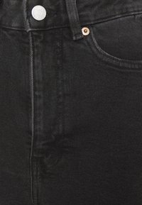 Jean en denim noir avec une taille haute, un bouton en métal et des surpiqûres visibles. La texture est lisse avec une légère brillance et une décoloration minimale.