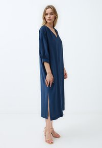 Abito midi blu navy con scollatura a V, maniche a palloncino e fessure laterali. Realizzato in un tessuto morbido, presenta una vestibilità comoda e una superficie liscia.