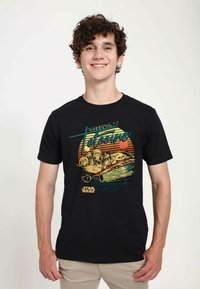 T-shirt en coton noir présentant une impression graphique d'un speeder dans une scène désertique avec le texte "Bienvenue à Tatooine" dans des couleurs rétro.