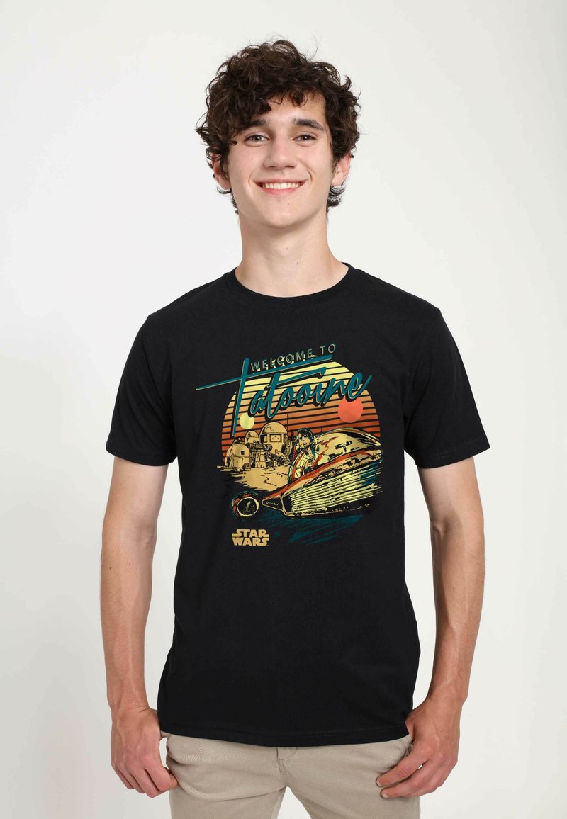 T-shirt en coton noir présentant une impression graphique d'un speeder dans une scène désertique avec le texte "Bienvenue à Tatooine" dans des couleurs rétro.