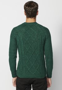 Groene gebreide trui met een getextureerd ruitpatroon en geribbelde manchetdetails. Beschikt over lange mouwen en een ronde halslijn.