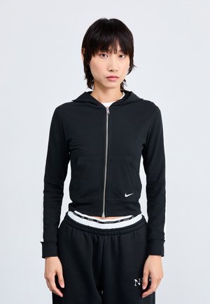 Black zip-up hoodie with a hood, front pocket, and white Nike logo. Features fitted sleeves and sporty design. Paired with black sweatpants.