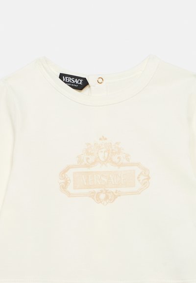 Άσπρο βαμβακερό t-shirt με ελαφρύ χρυσαφί λογότυπο Versace στο μπροστινό μέρος, στρογγυλή λαιμόκοψη και κλείσιμο με κουμπιά στην πλάτη.