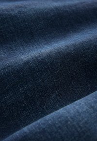 Donkerblauwe denimstof met een zachte textuur, gekenmerkt door een lichte glans en een diagonale weefpatroon. Het oppervlak vertoont zachte variaties in schaduw.