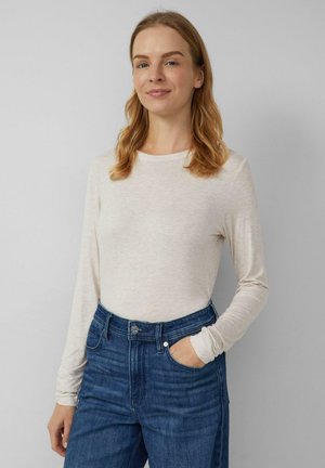 Hellbeiges Langarmshirt aus weichem Stoff, kombiniert mit hoch taillierten, dunkelblauen Denim-Jeans. Das Oberteil hat einen einfachen, runden Ausschnitt.