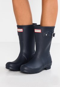 Bottes de pluie en caoutchouc bleu marine avec un design mi-mollet, dotées d'une accentuation par boucle, d'une texture lisse et d'un logo de marque près du haut.