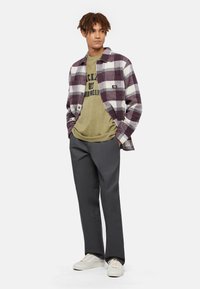 Skjorte med tern i lilla og hvid, olivengrøn t-shirt med tryk, grå bukser og hvide sneakers. Afslappet outfit med kontrasterende teksturer.