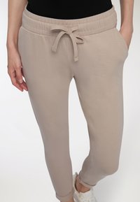 Beżowe joggery zwężane z elastycznym paskiem w talii i sznurkiem, z bocznymi kieszeniami i gładką, miękką teksturą.